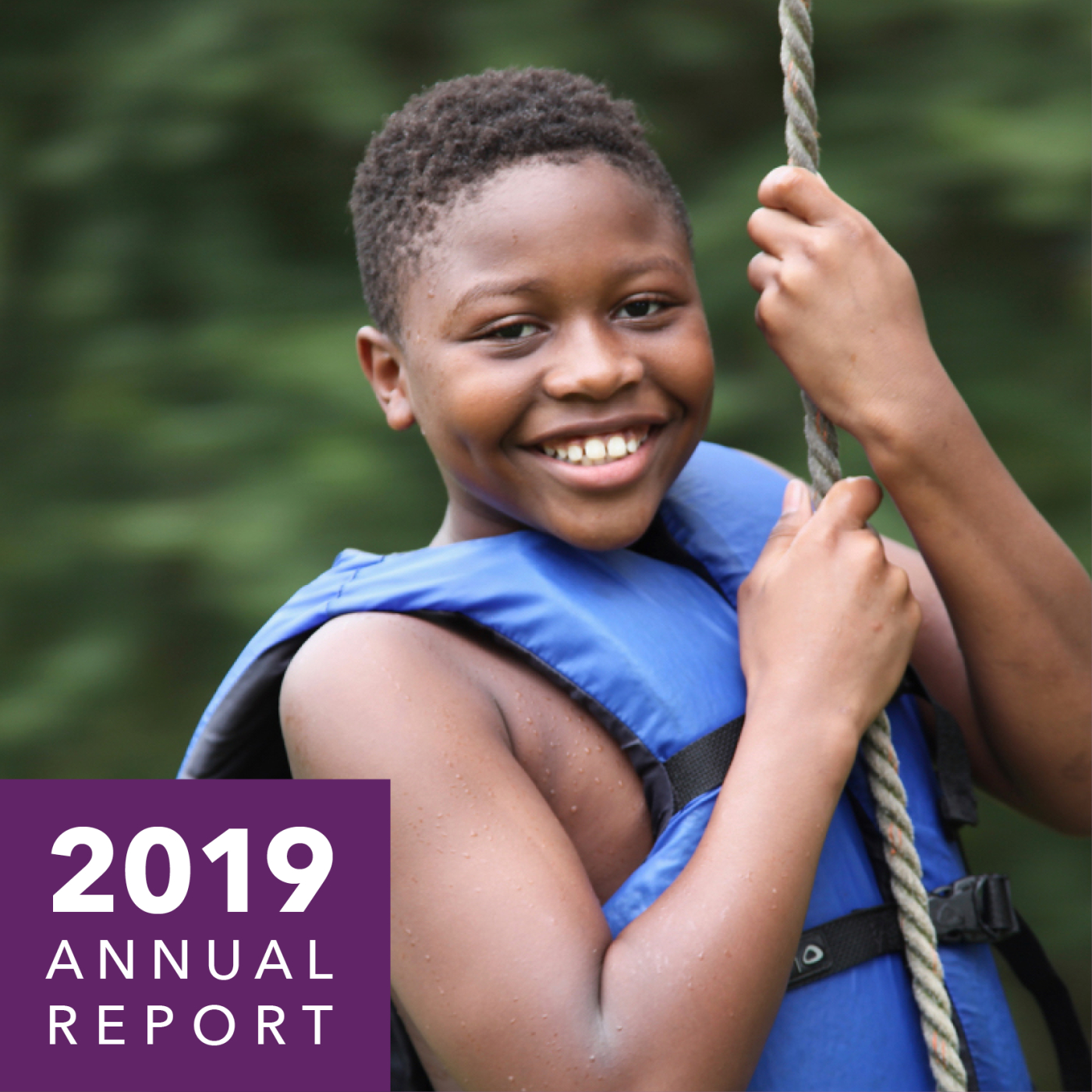 A child in a lifejacket holds onto a rope and smiles.