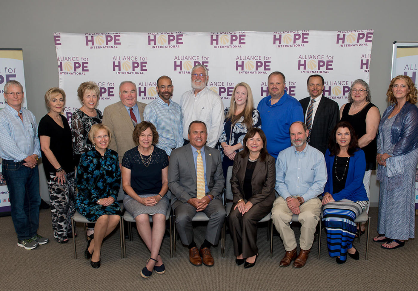 A group of people poses for a formal photo in front of a backdrop displaying the 'Alliance for HOPE International' logo
