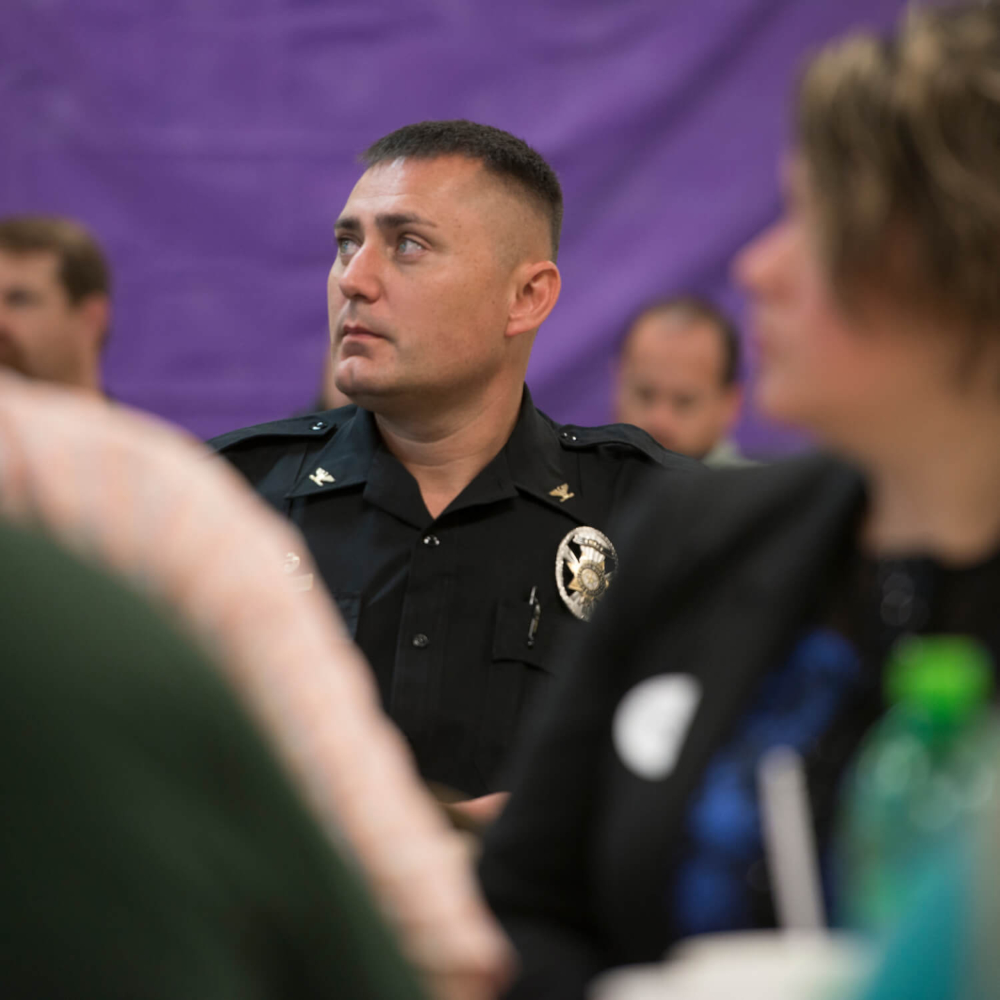 A uniformed police officer attentively listens during a training event, surrounded by other attendees in a conference setting.